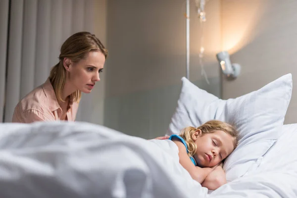 Preoccupato madre guardando malato bambino dormire sul letto in ospedale — Foto stock