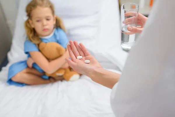 Cropped image of doctor holding pills and water for child patient — Stock Photo