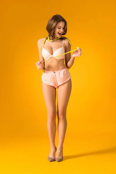 Surprised sexy girl in lingerie set looking at tape measure on orange — Stock Photo