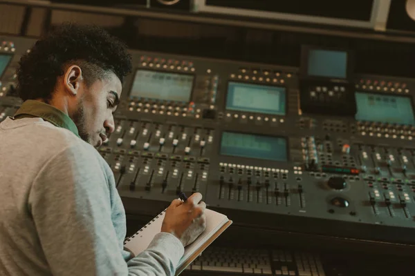 Beau jeune musicien écrivant dans un cahier au studio d'enregistrement — Photo de stock