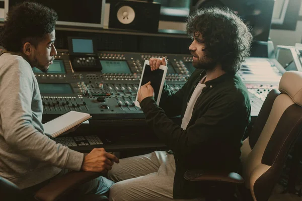 Hombre mostrando pantalla de tableta en blanco al productor de sonido en el estudio de grabación - foto de stock