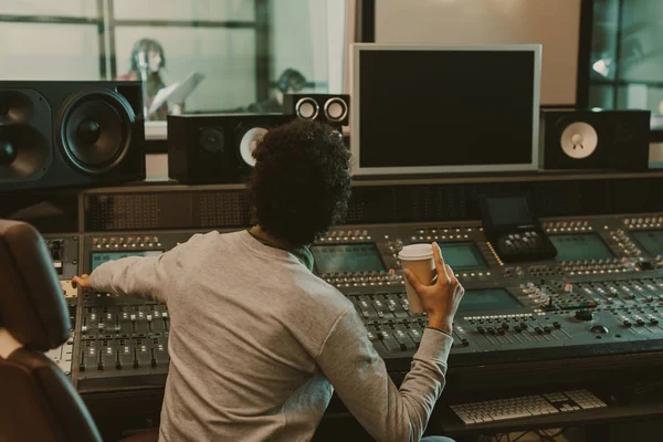 Produtor de som com copo descartável de café trabalhando no estúdio — Fotografia de Stock