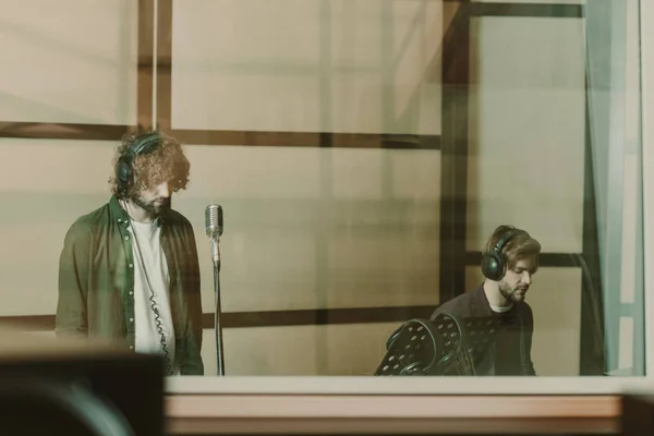 Groupe de deux musiciens encodage chanson derrière verre au studio — Photo de stock