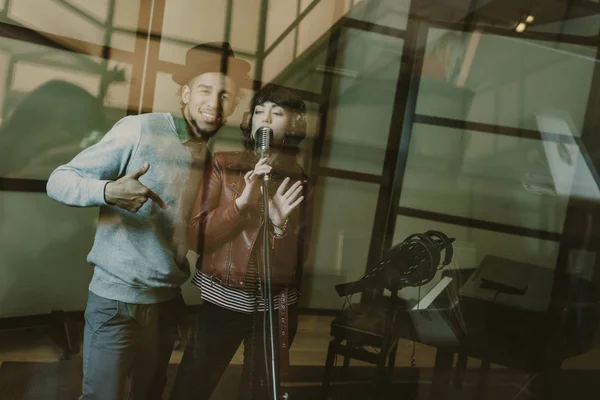 Young singers couple recording song behind glass at studio — Stock Photo