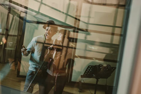Jeunes chanteurs talentueux couple enregistrement chanson derrière verre au studio — Photo de stock