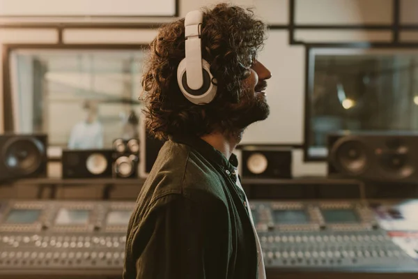 Vista lateral del productor de sonido en auriculares disfrutando de la música en el estudio - foto de stock