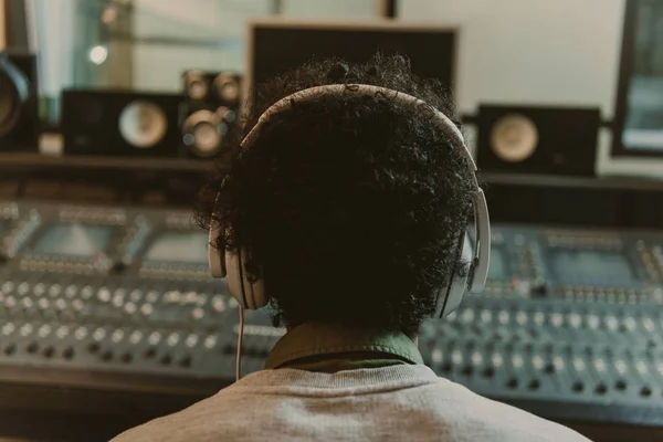 Back view of sound producer in headphones sitting at studio — Stock Photo