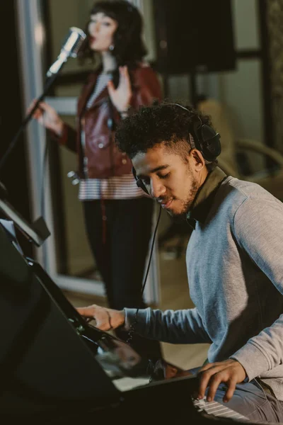 Jovem músico afro-americano tocando piani enquanto cantor tocando música no fundo — Fotografia de Stock