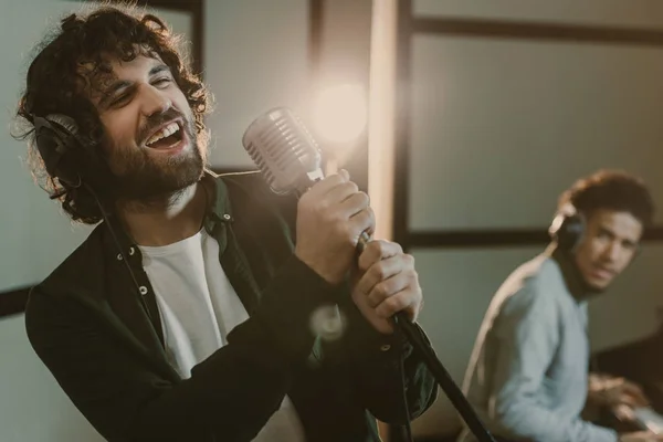 Jeune homme artistique exécutant la chanson avec microphone tandis que l'homme jouant du piano flou sur fond — Photo de stock