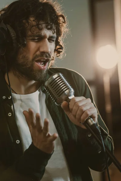 Emocional joven cantante en auriculares cantando canción en el estudio - foto de stock