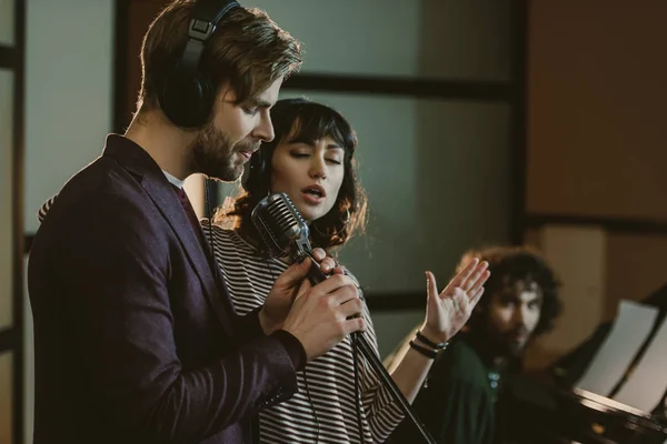 Cantanti che eseguono canzoni mentre l'uomo suona il pianoforte dietro — Foto stock