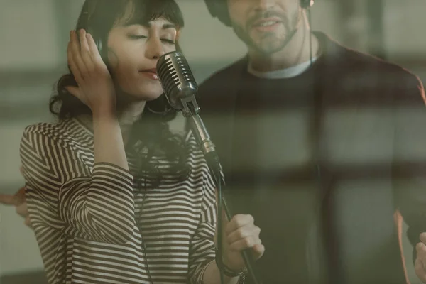 Cantores jovens cantando música atrás de vidro no estúdio de gravação — Fotografia de Stock