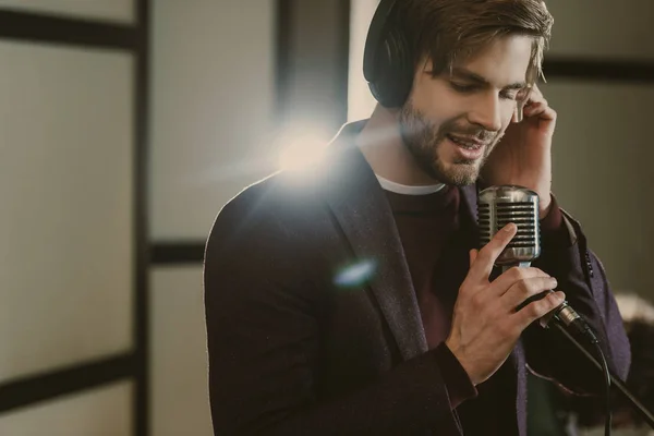 Guapo joven cantante en auriculares cantando canción en el estudio - foto de stock