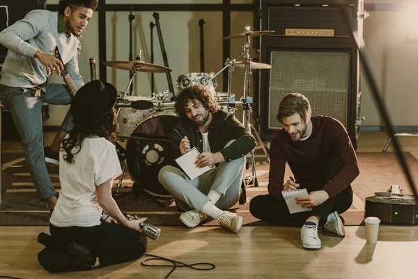 Jeune groupe de musique assis sur le sol et la création de texte pour la chanson ensemble — Stock Photo