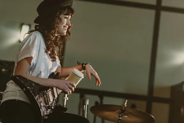 Hermosa mujer músico con guitarra eléctrica y taza de café para llevar - foto de stock