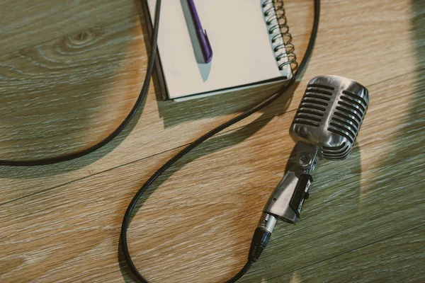 Top view of wired vintage microphone lying on wooden table with blank notebook — Stock Photo