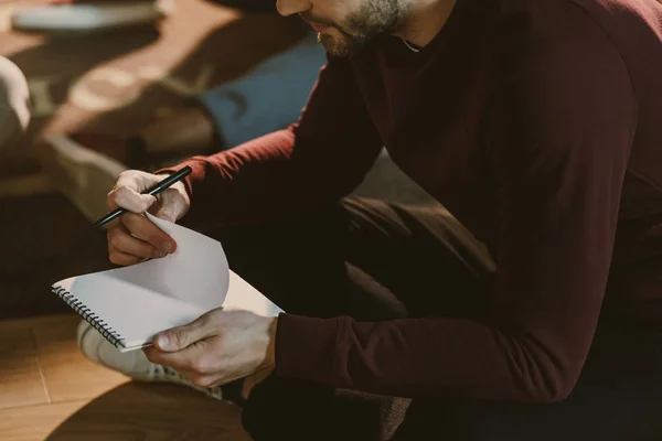 Recortado disparo de guapo joven sosteniendo bloc de notas en blanco — Stock Photo