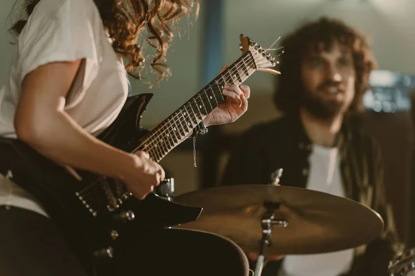 Tiro recortado de guitarrista feminino executando música com baterista desfocado no fundo — Fotografia de Stock