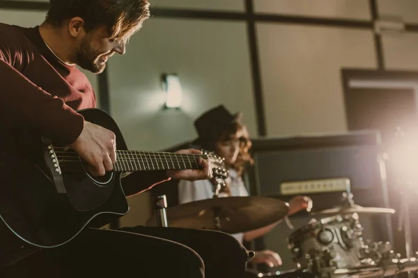 Schöne junge Musikerin spielt Gitarre in der Wiederholung mit verschwommener Schlagzeugerin im Hintergrund — Stockfoto