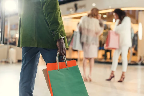 Recortado disparo de hombre afroamericano sosteniendo bolsas de papel mientras camina en el centro comercial - foto de stock