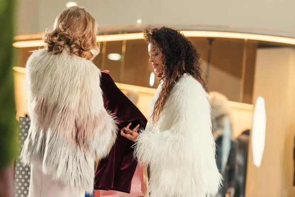 Femmes multiethniques à la mode en manteaux de fourrure faisant du shopping ensemble dans un centre commercial — Photo de stock