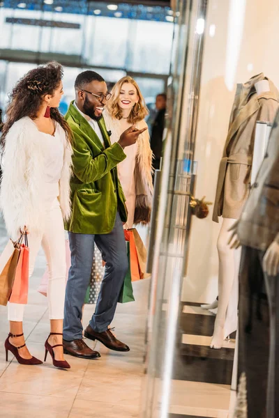 Vue de côté des gens souriants multiethniques à la mode faisant du shopping ensemble dans le centre commercial — Photo de stock