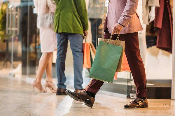 Low section of stylish man with shopping bags walking nd couple standing behind in mall — Stock Photo