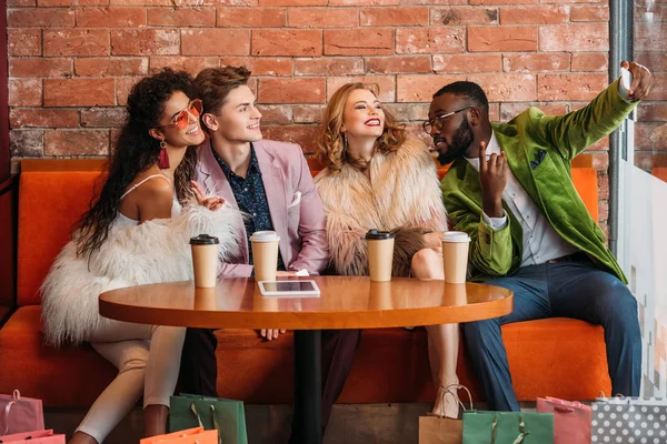 Sonrientes compradores jóvenes multiétnicos de moda tomando selfie con teléfono inteligente - foto de stock