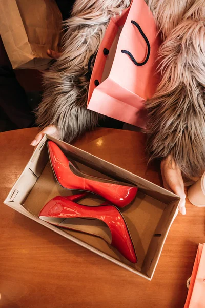 Tiro recortado de mujer con estilo en abrigo de piel caja de espera con zapatos de tacón alto rojo de moda - foto de stock