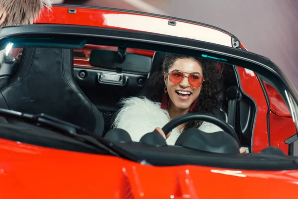 Happy stylish young african american woman in fur coat driving luxury luxury car — Stock Photo