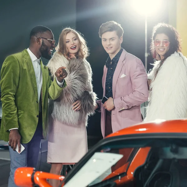 Giovani multietnici alla moda guardando auto rossa moderna — Foto stock