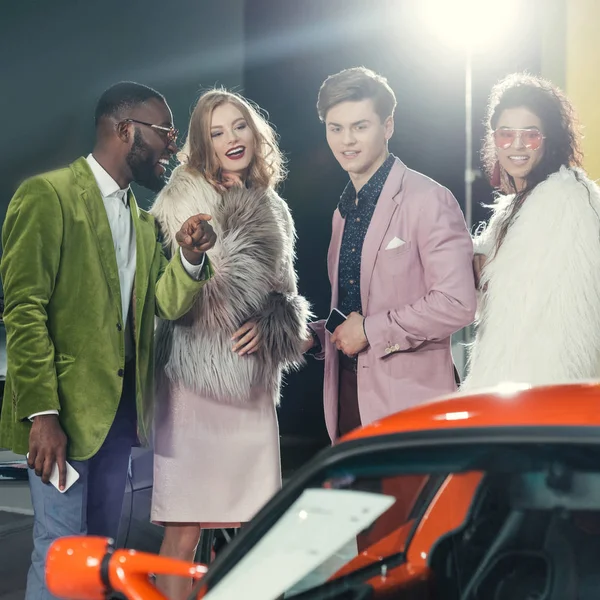 Stylish multiethnic young people looking at modern red car — Stock Photo