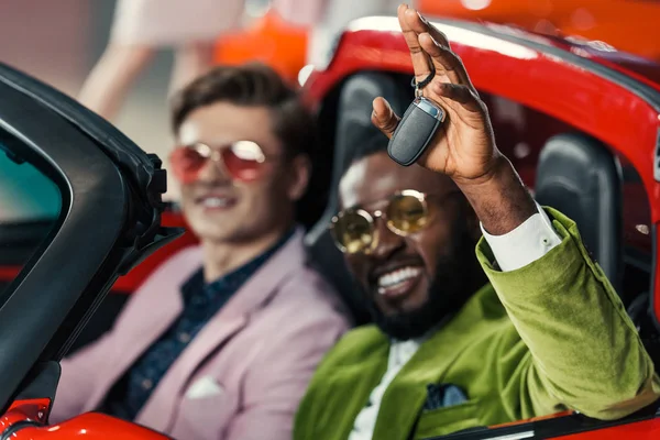 Beaux hommes élégants avec clé de voiture assis dans une nouvelle voiture au showroom — Photo de stock