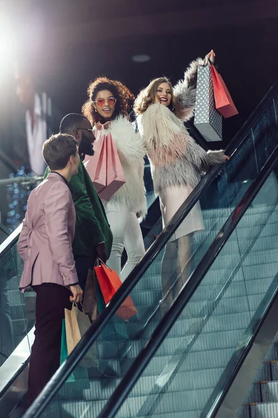Grupo joven y elegante de compradores en escaleras mecánicas en el centro comercial - foto de stock
