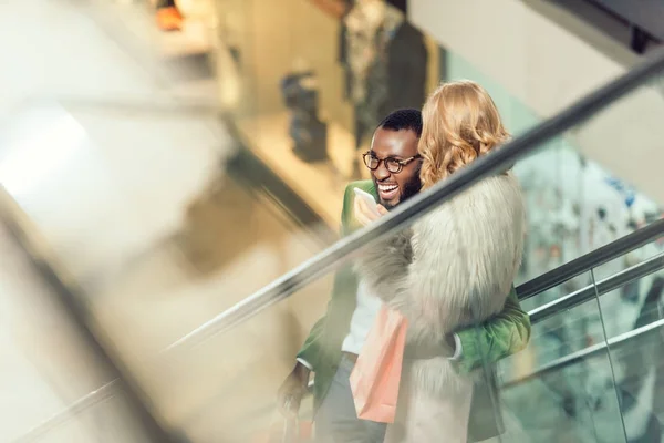 Stylish young couple riding escalator and embracing at shopping mall — Stock Photo