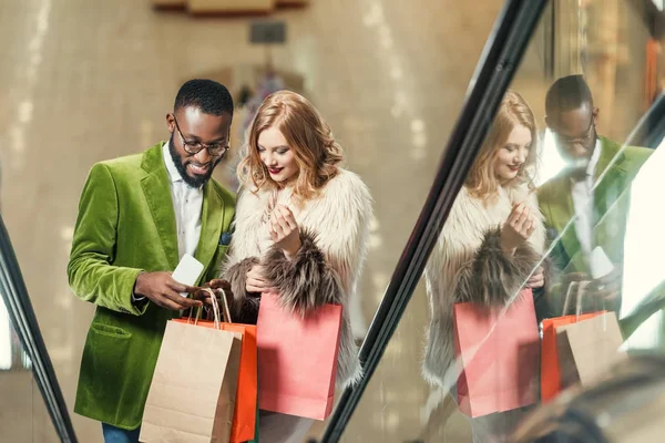 Felice giovane coppia cavalcando scala mobile al centro commerciale — Foto stock