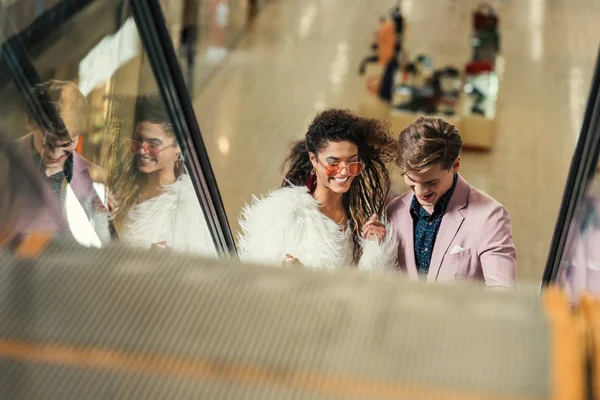Giovane coppia cavalcando scala mobile al centro commerciale — Foto stock