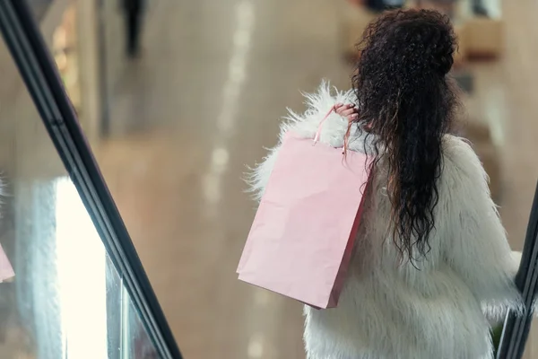 Visão traseira da mulher elegante segurando saco de compras enquanto montando escada rolante — Fotografia de Stock