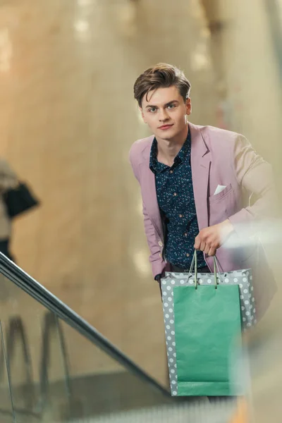 Hombre con estilo en escaleras mecánicas con bolsas en el centro comercial - foto de stock