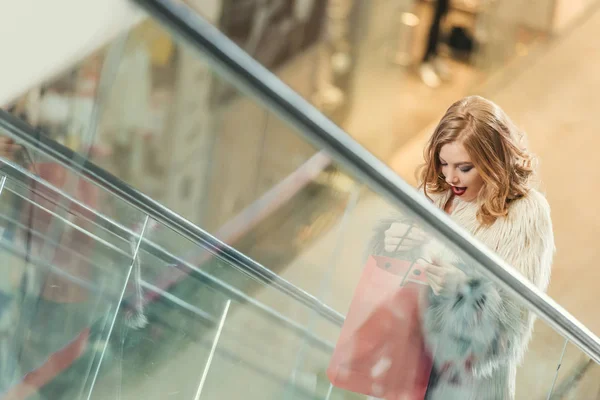 Mujer sorprendida con bolsa de compras montar escaleras mecánicas - foto de stock