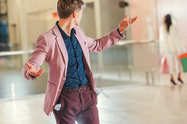 Stylish young man with empty pockets turning back on girlfriend while she walking away at shopping mall — Stock Photo