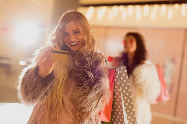Smiling young woman in fur coat with golden credit card on shopping — Stock Photo
