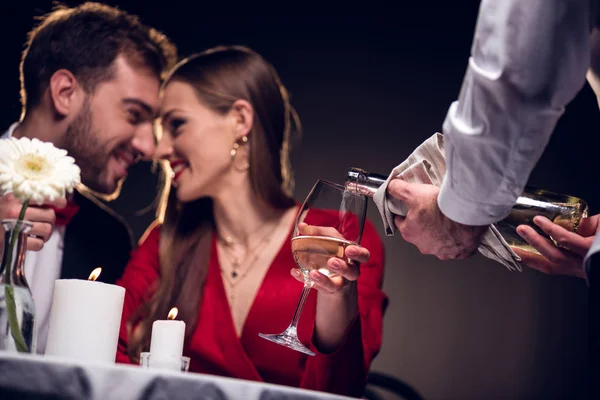 Camarero vertiendo vino mientras sonríe pareja teniendo una cita romántica en el restaurante el día de San Valentín - foto de stock