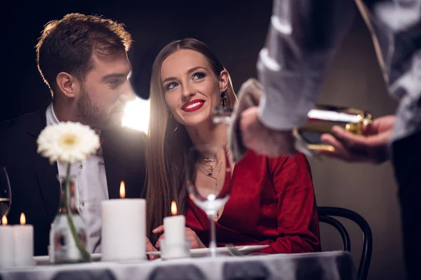 Garçom derramando vinho enquanto casal feliz ter data romântica no restaurante no dia dos namorados — Fotografia de Stock