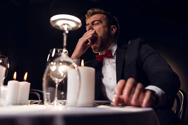 Hombre cansado bostezando y esperando una cita romántica en el restaurante - foto de stock
