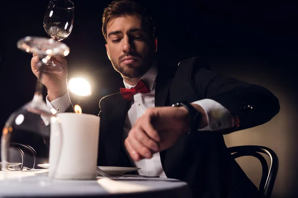 Красивый бородатый мужчина смотрит на часы в ожидании романтического свидания в ресторане — стоковое фото
