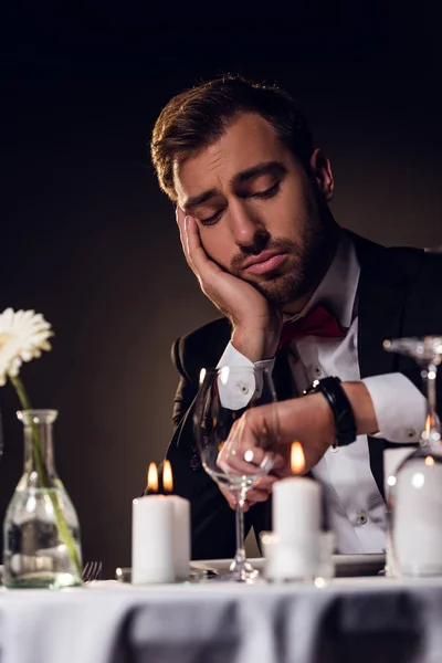 Müder Mann schaut auf Uhr, während er auf ein romantisches Date im Restaurant wartet — Stockfoto