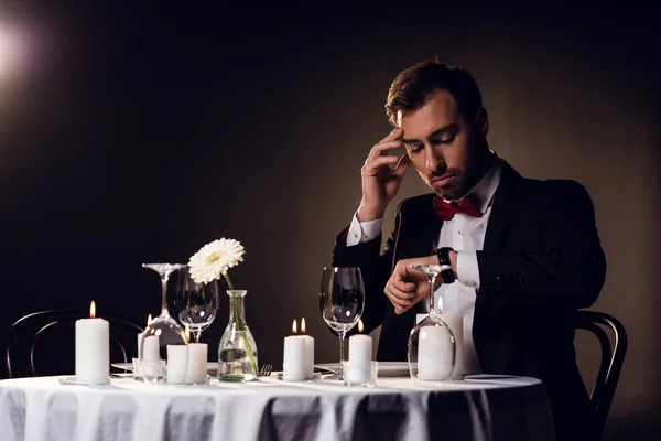 Besorgter Mann schaut auf Uhr, während er auf romantisches Date im Restaurant wartet — Stockfoto