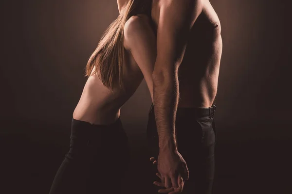 Cropped view of couple standing back to back and holding hands, isolated on brown — Stock Photo