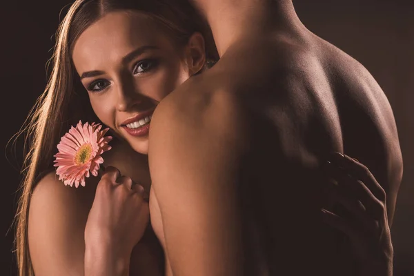 Casal nu abraçando e segurando flor, isolado em marrom — Fotografia de Stock